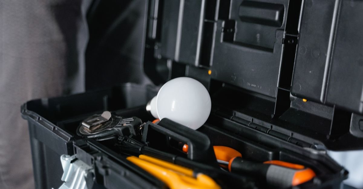 Open black equipment case containing orange-handled tools, a coiled cable, and a white light bulb.