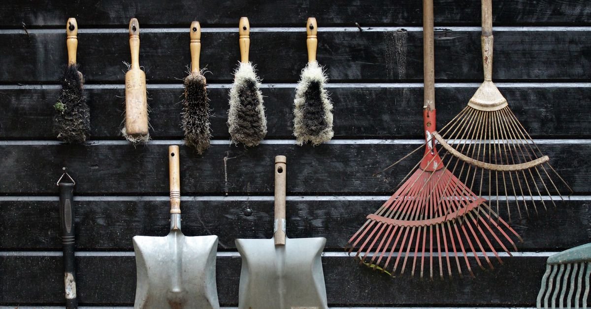Garden tools, brushes, shovels and rakes hanging neatly on a dark wooden wall.