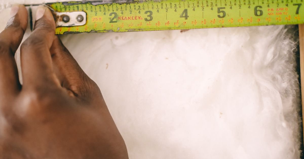 A hand holds a measuring tape across a white, fluffy material.