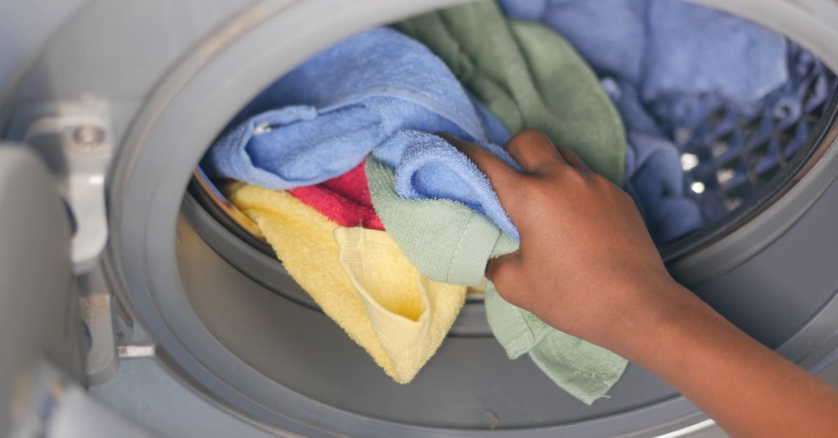 A hand removes colorful towels from the open door of a front-loading washing machine.
