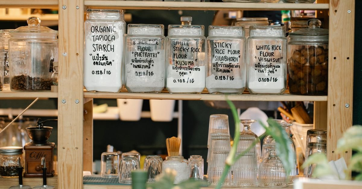 Glass jars of labeled rice and tapioca flours sit on wooden shelves alongside other pantry containers and kitchenware.