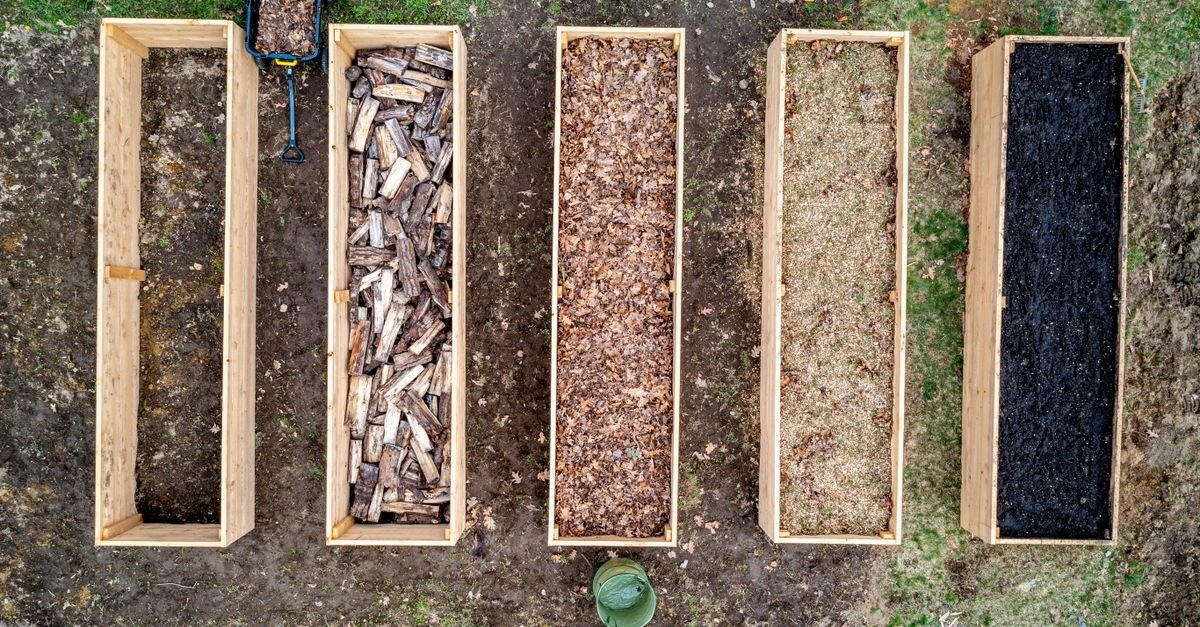 Overhead view of five wooden garden beds filled with soil, logs, leaf mulch, pale wood chips, and dark compost.