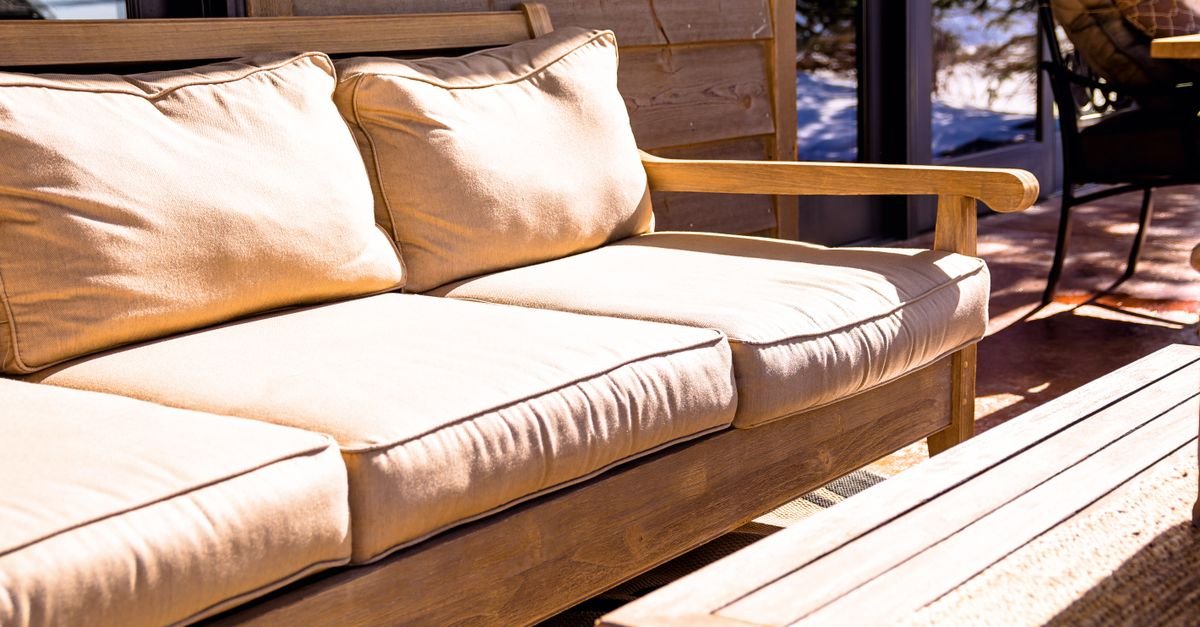 Outdoor wooden sofa with beige cushions beside a wooden table in bright sunlight.